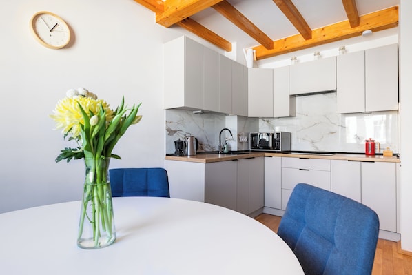 A modern kitchen with white cabinets, a marble countertop, and a clock on the wall.