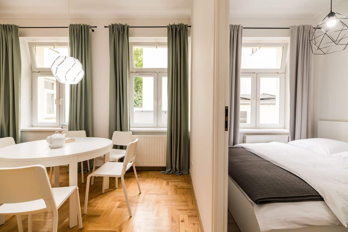 Une pièce comprenant un lit, une table ronde avec des chaises et une fenêtre avec des rideaux.