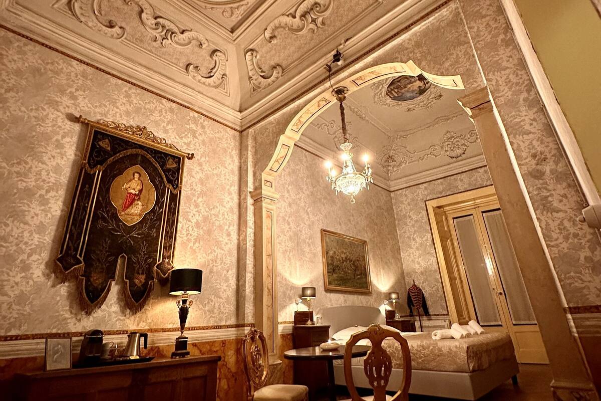 Ein luxuriöser Raum mit aufwändigen Deckenverzierungen, einem Chandelier, einem Bett und einem Schreibtisch mit Lampe.