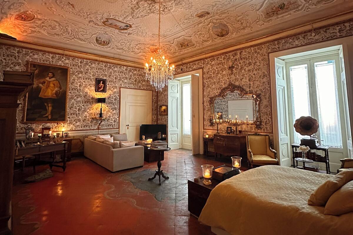 Ein luxuriöses Schlafzimmer mit aufwendiger Deckenverzierungen, einem großen Bett, einer Sitzecke und einem Esstisch.