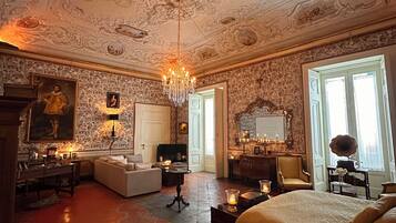 Un dormitorio lujoso con techo ornamentado, una cama grande, una zona de estar y una mesa de comedor.