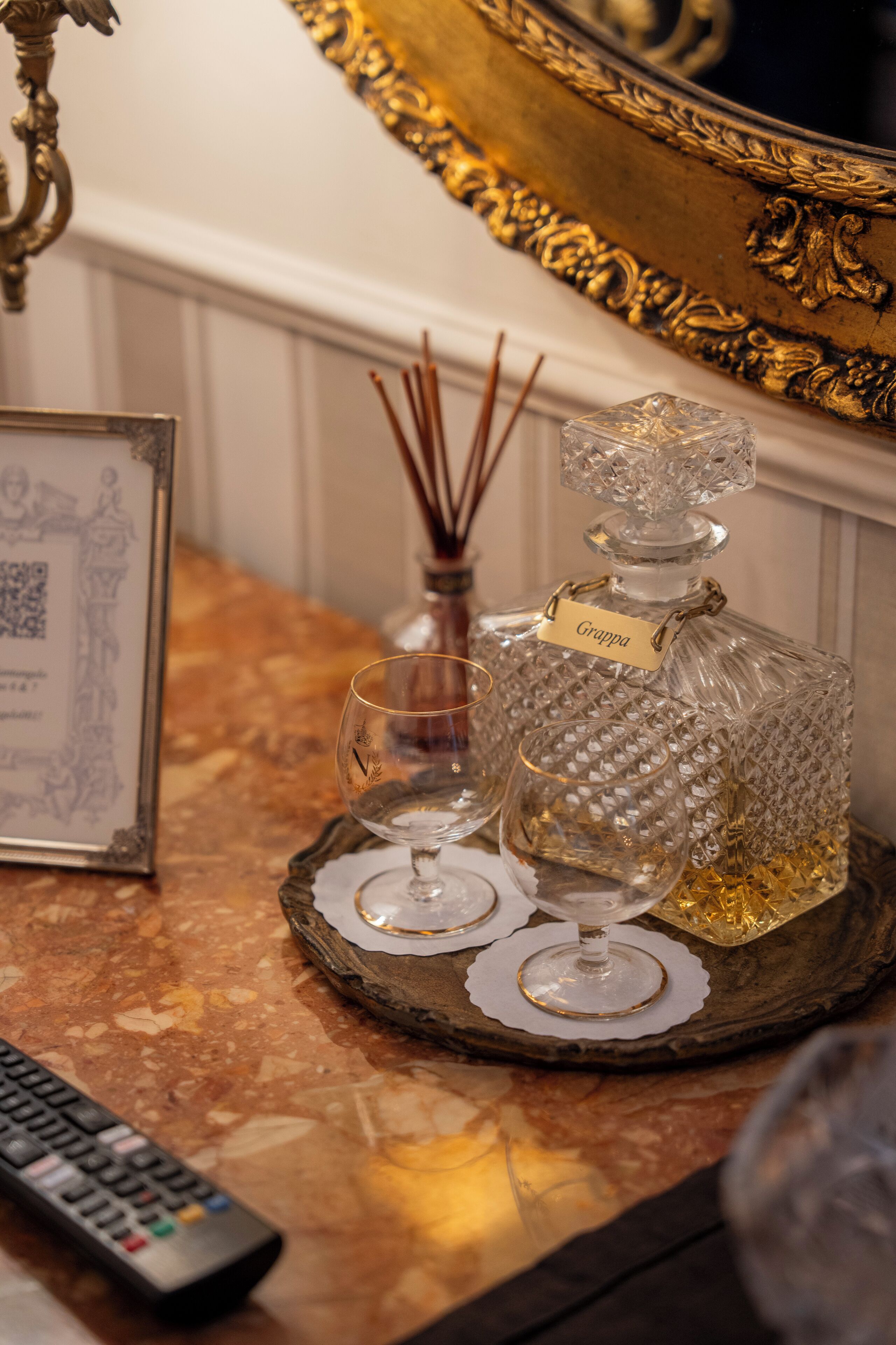 A tray with a crystal decanter labeled "Grappa," a glass, and a remote control on a marble surface.