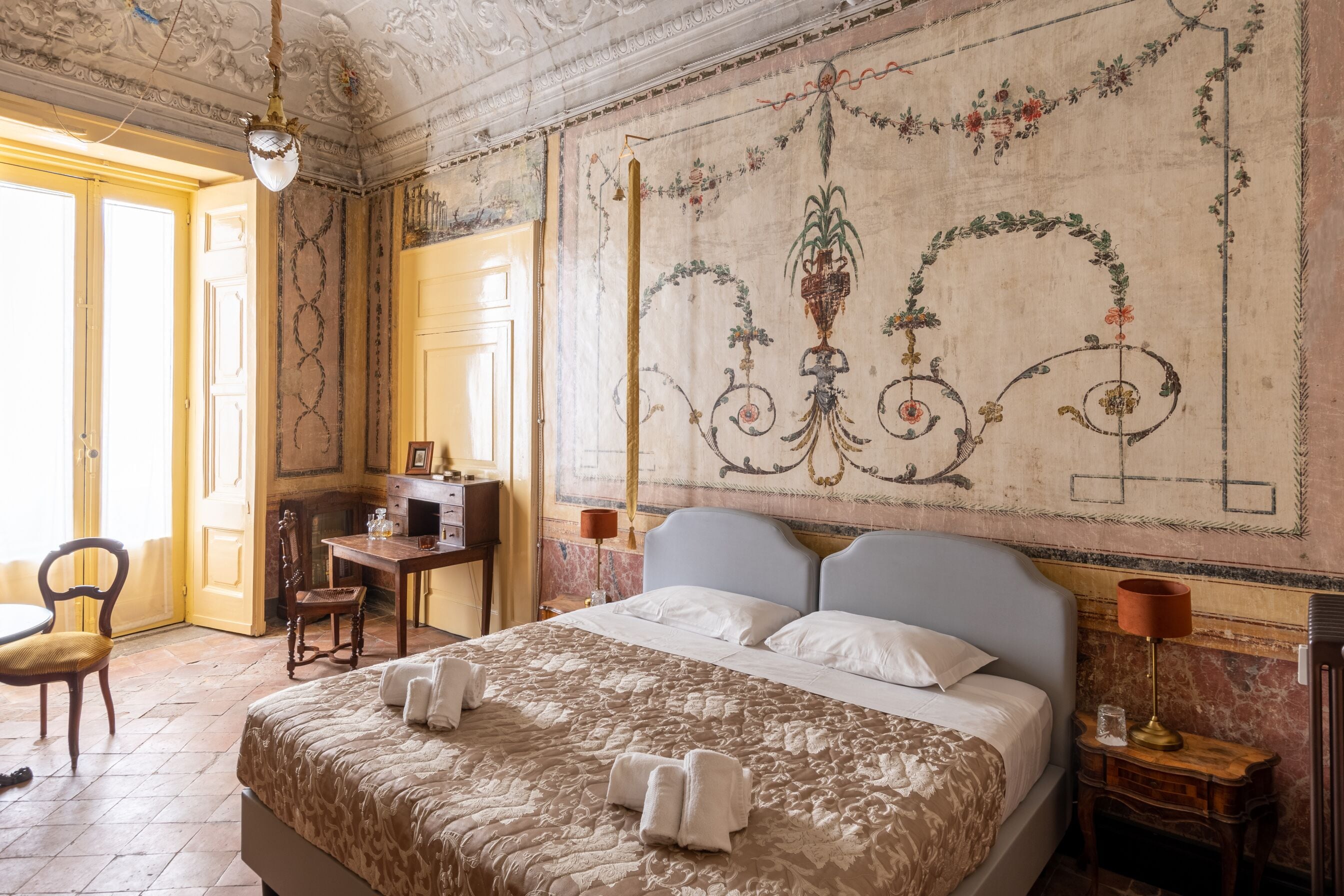 A hotel room with a large bed, a desk, a chair, and a decorative wall mural.