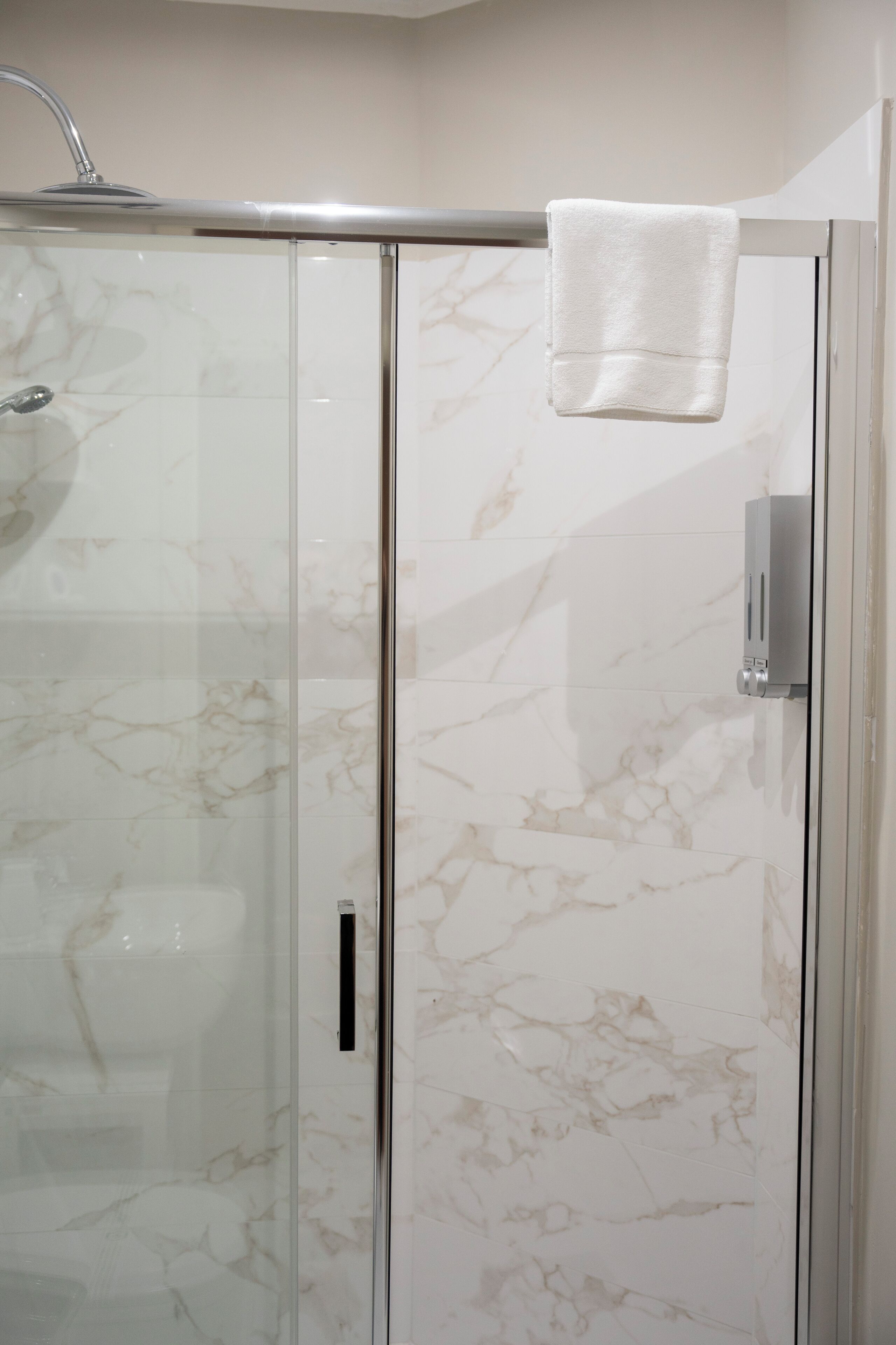 Une douche fermée par des parois de verre, avec un mur en marbre et une serviette accrochée à la porte.