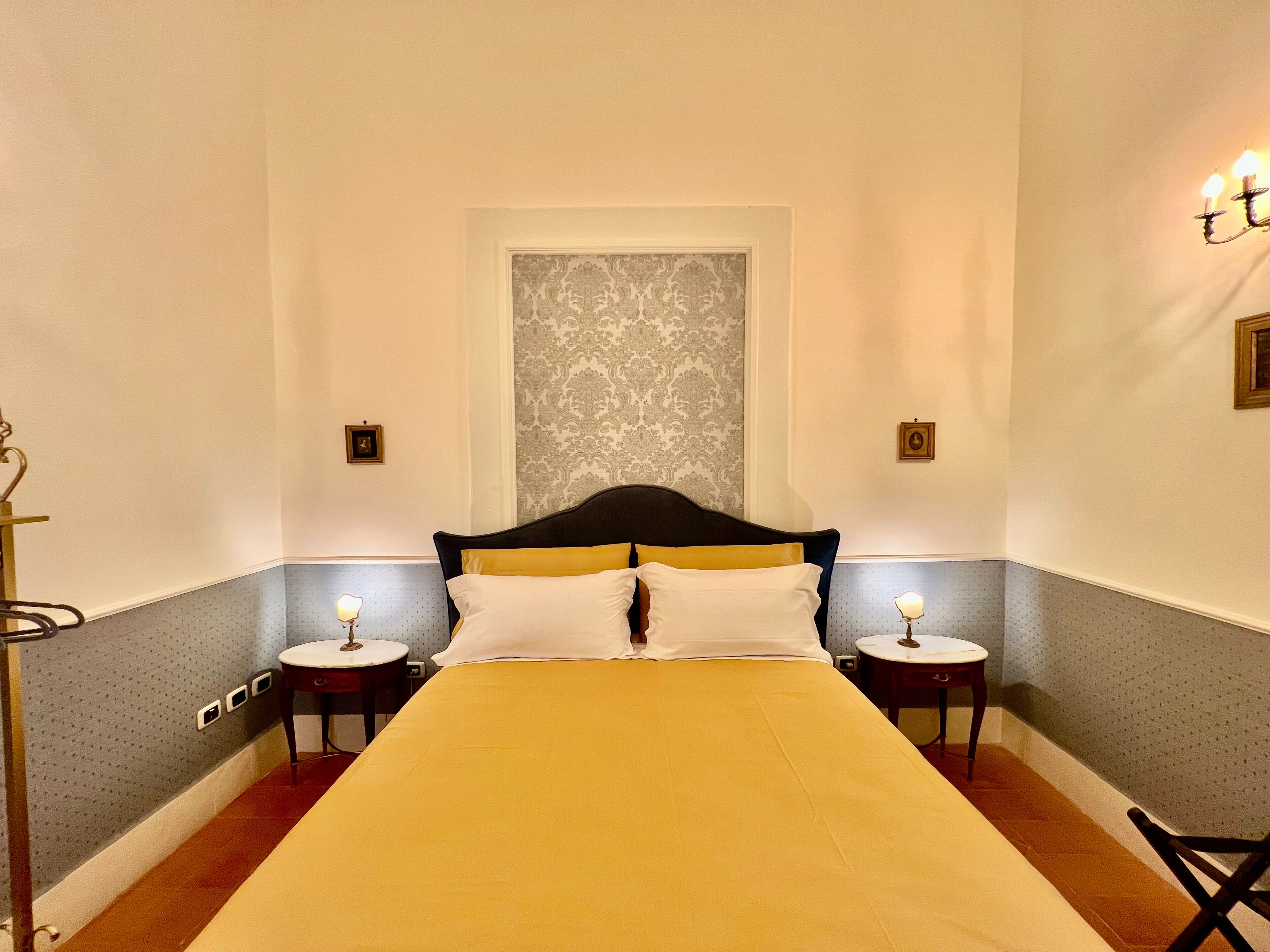 A hotel room with a large bed, two bedside tables, a chair, and a wall with a decorative pattern.