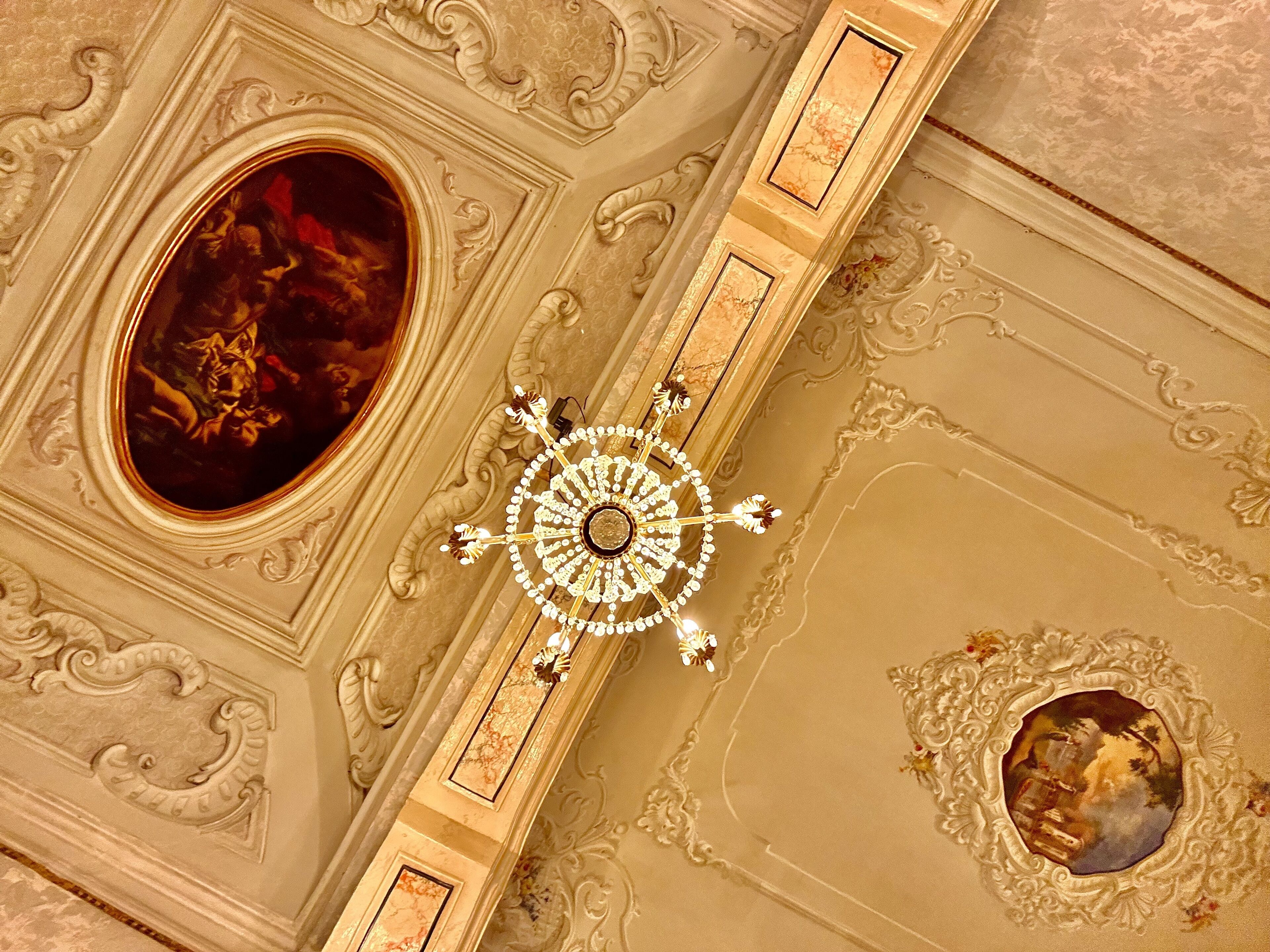 Techo con molduras ornamentales, un candelabro y dos cuadros ovalados.