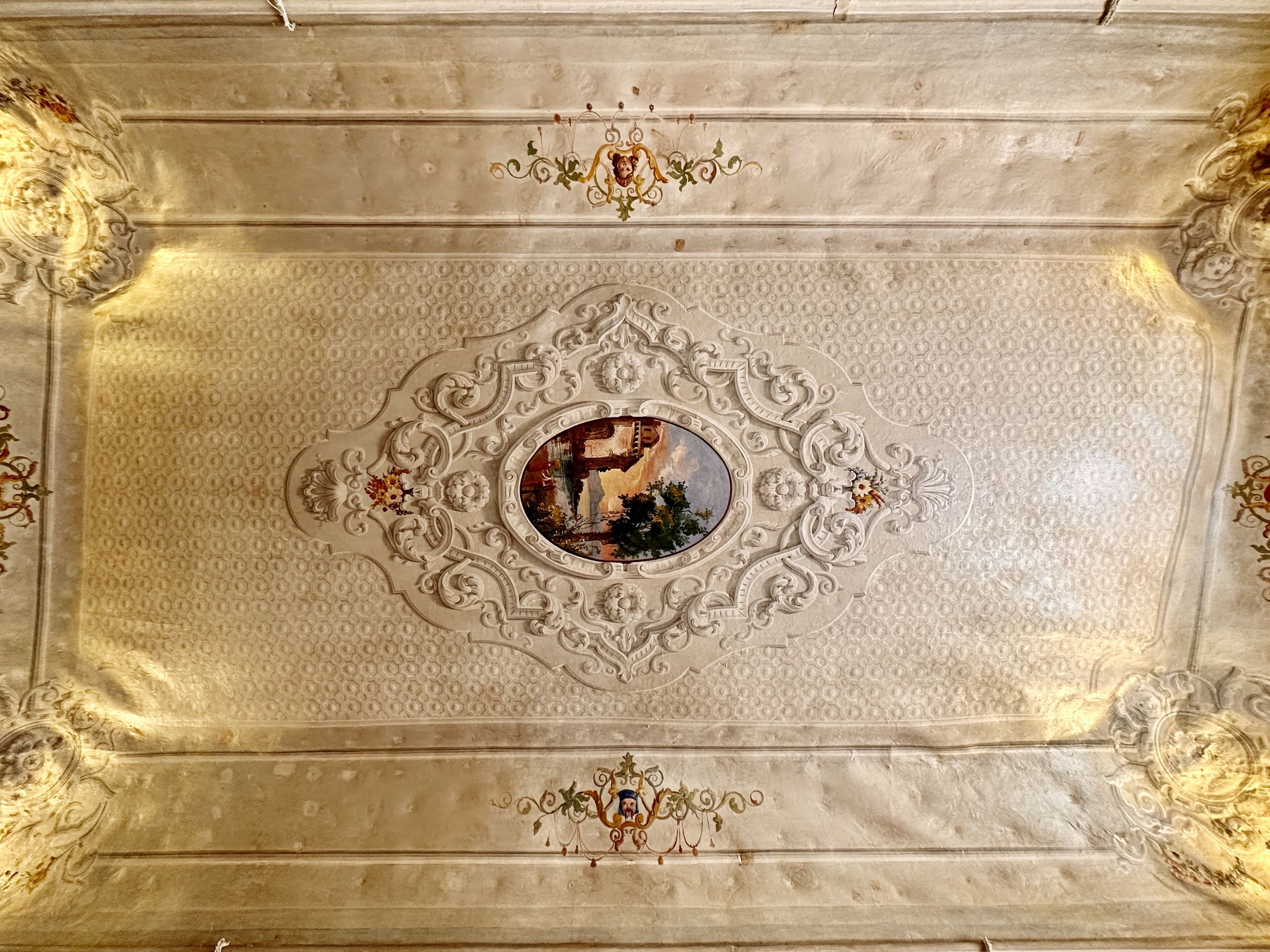 A ceiling with intricate carvings and a central oval mirror.
