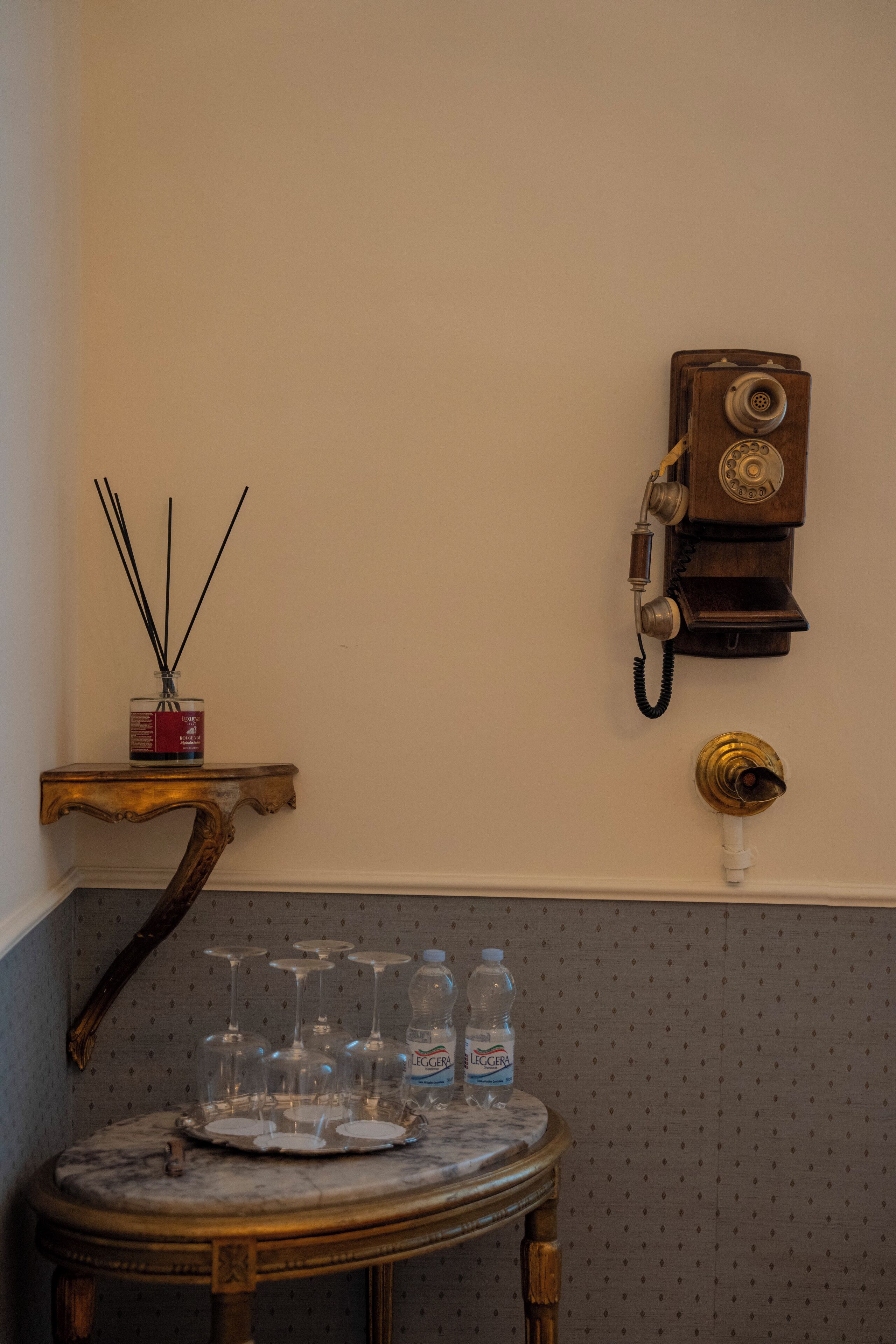 Un vieux téléphone, une petite table avec un plateau de verres et deux bouteilles d’eau sur une étagère fixée au mur.