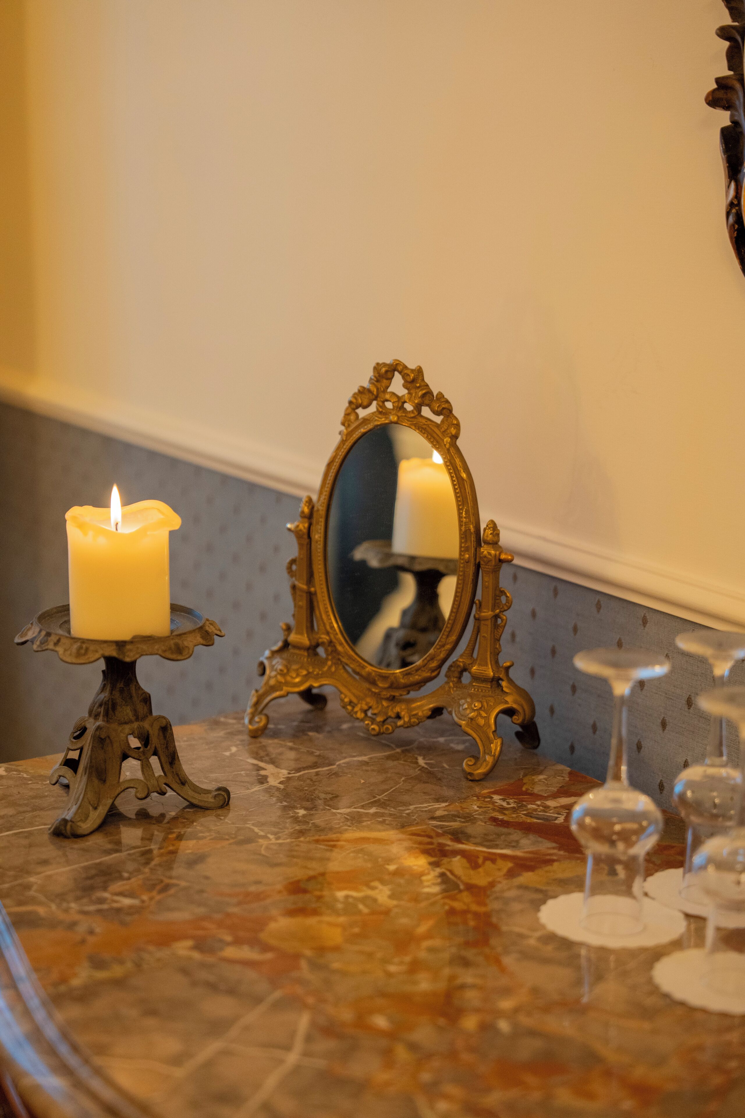 A candle on a stand, a mirror, and wine glasses on a marble surface.