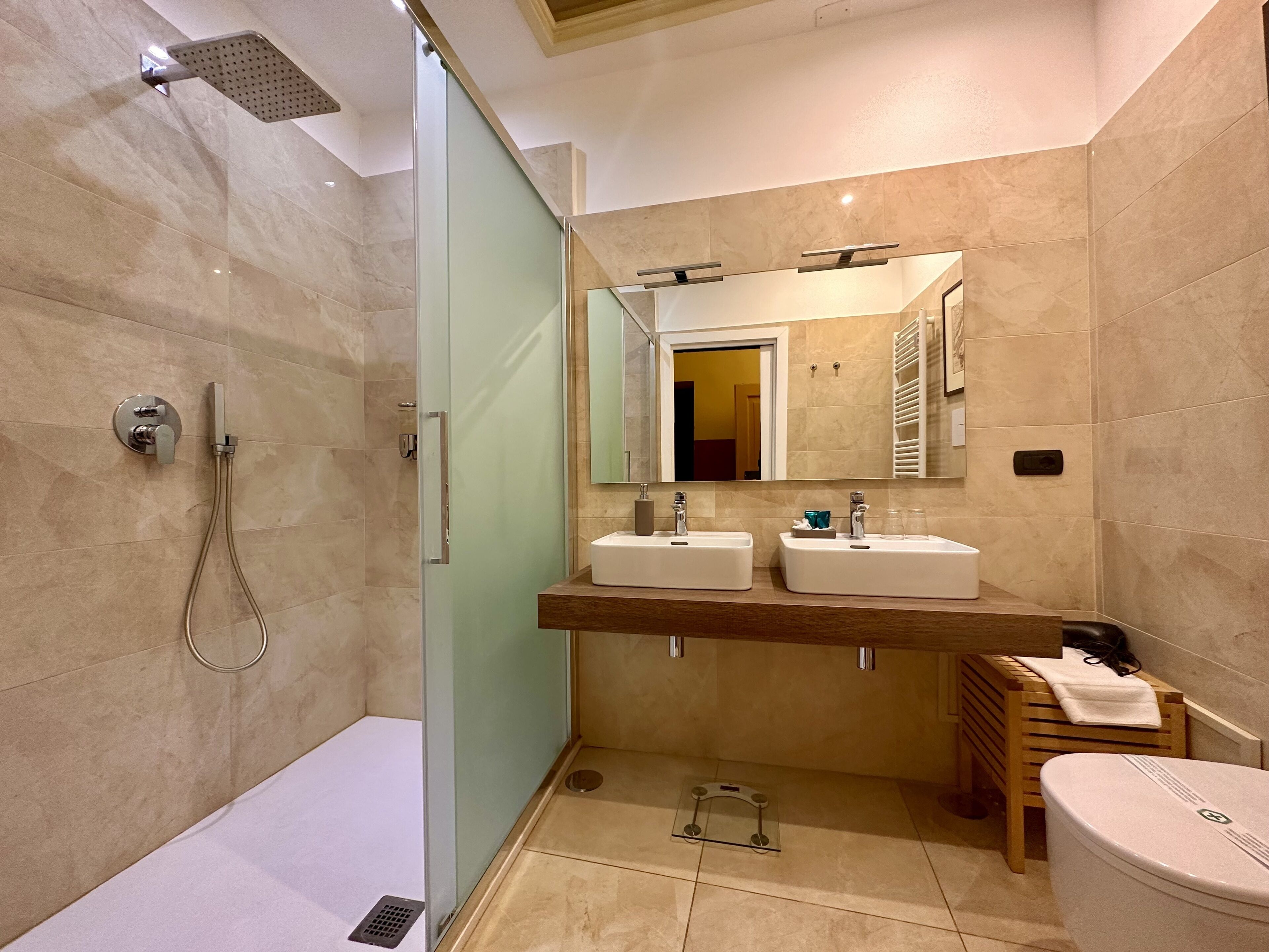 A modern bathroom with a glass-enclosed shower, two sinks, a mirror, and a toilet.