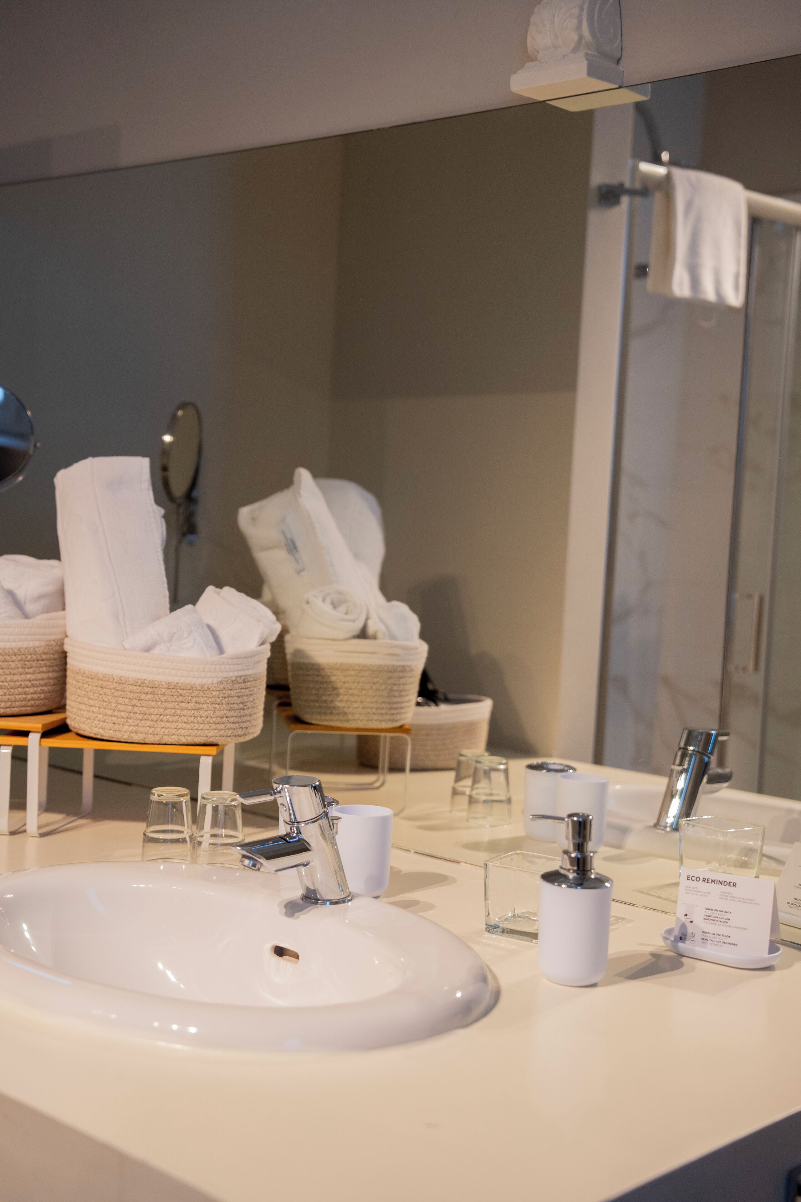 A modern bathroom with a large sink, two towel dispensers, and a glass shower enclosure.
