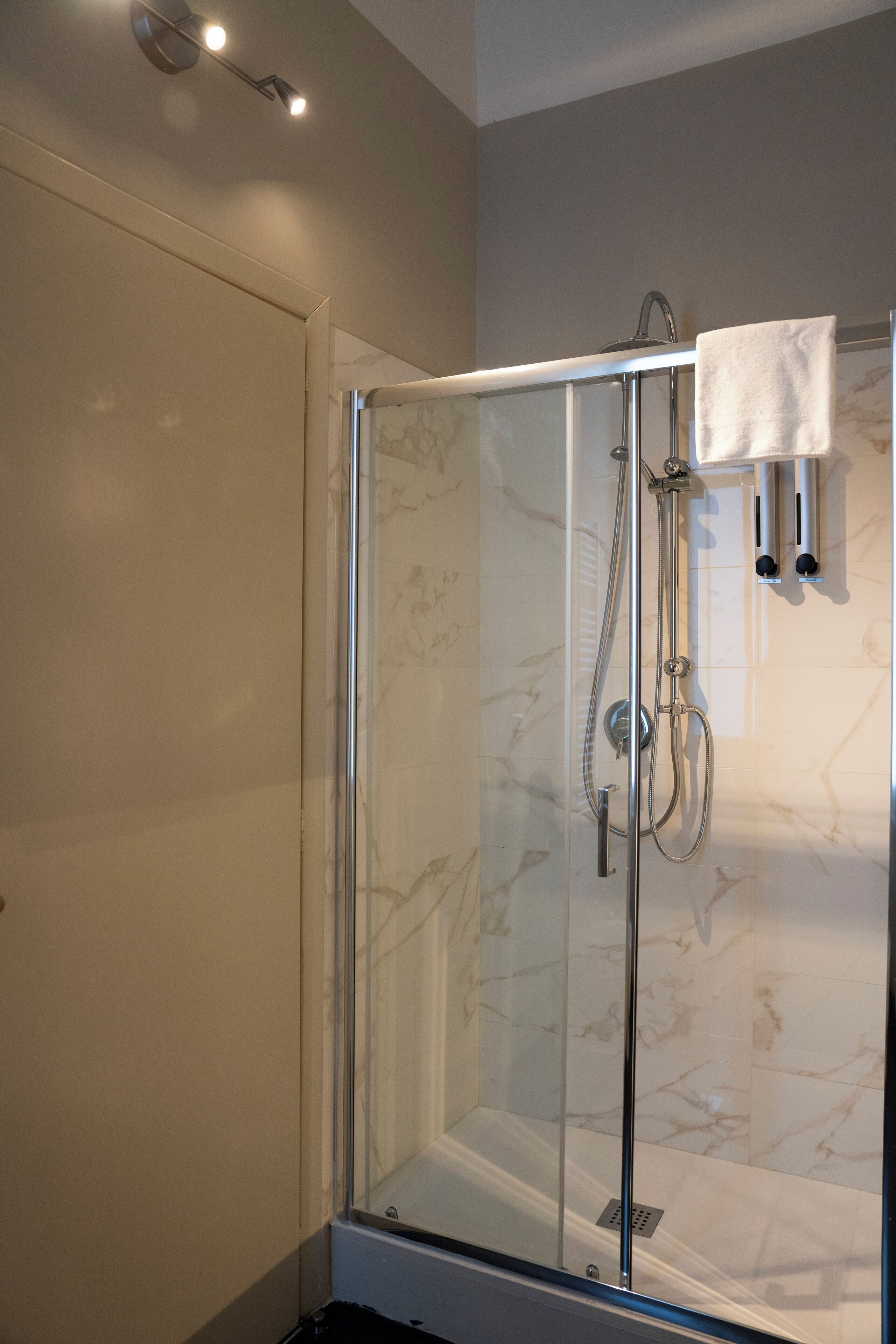 Une douche fermée par des parois en verre, dotée d’un pommeau de douche à main et d’un robinet mural.