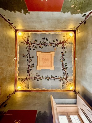 Una habitación con techo decorativo, una obra de arte enmarcada y una escalera.