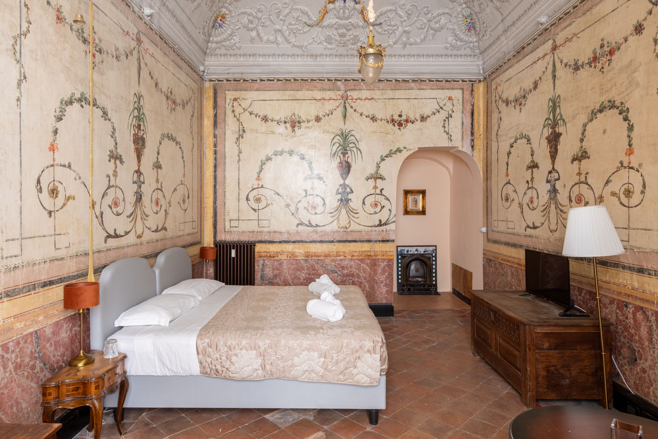 A room with a large bed, a wooden desk, a fireplace, and ornate wall decorations.
