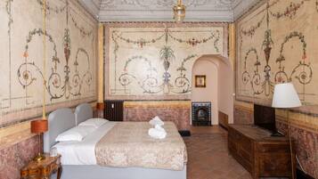 A room with a large bed, a wooden desk, a fireplace, and ornate wall decorations.