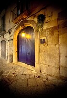 A dark blue door with a lit lantern above it, set in a stone building with a small plaque on the wall.