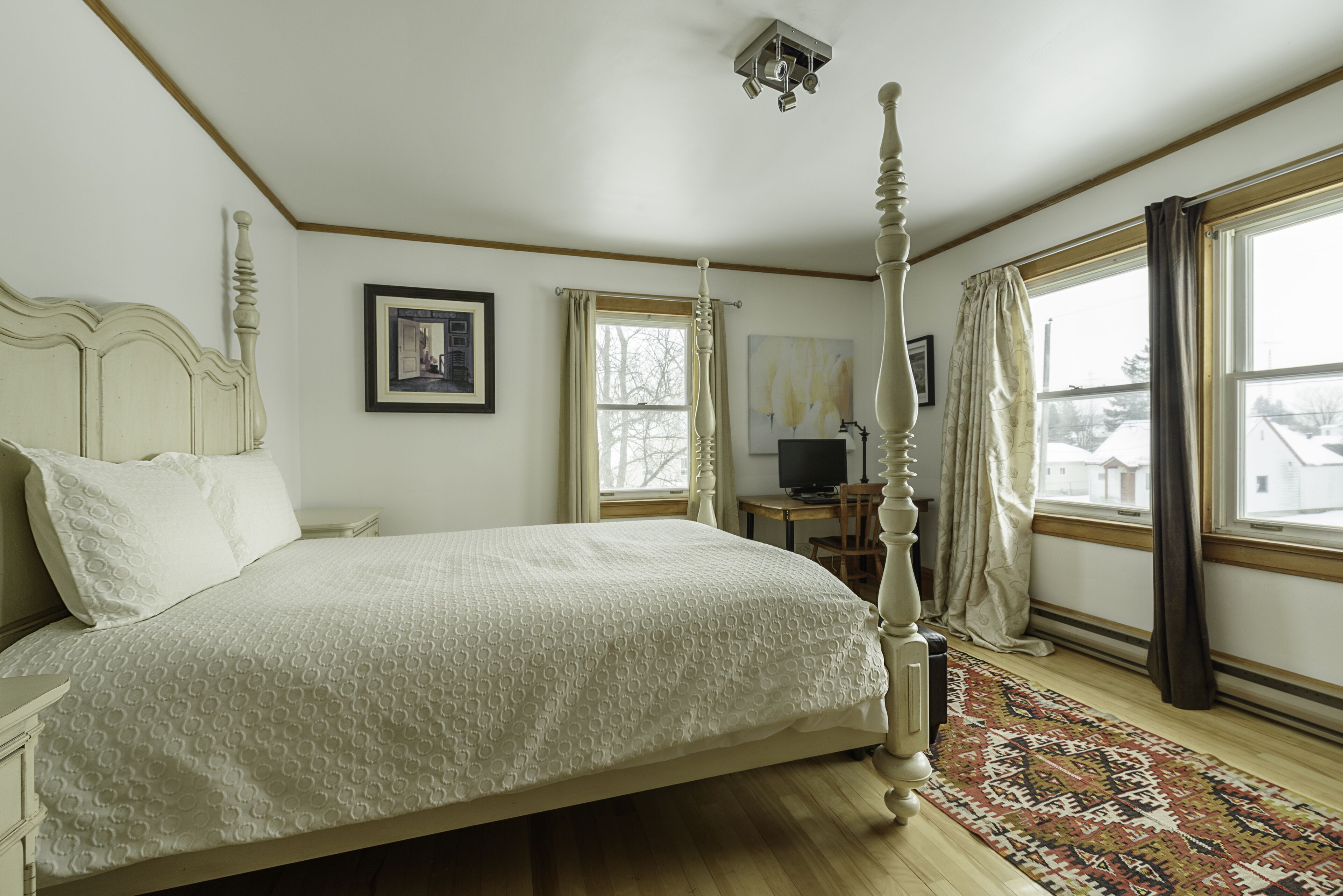 Une chambre à coucher avec un lit à baldaquin, un plancher en bois, une fenêtre avec des rideaux, un bureau avec une chaise et un téléviseur.