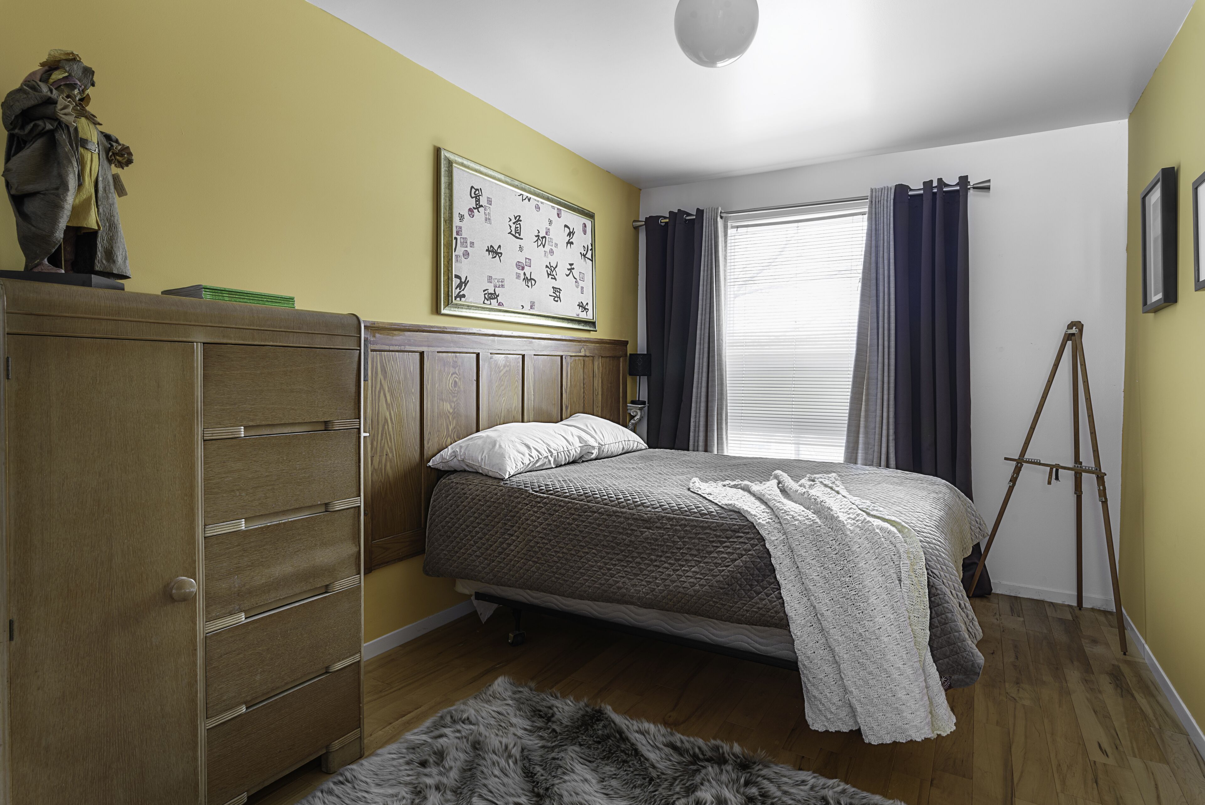 A bedroom with a bed, wooden dresser, and a framed artwork on the wall.