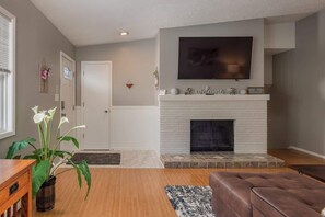 A living room with a fireplace, a television mounted above it, and a door to the left. - Downtown WestChester Casa with King Beds (Anchorage)