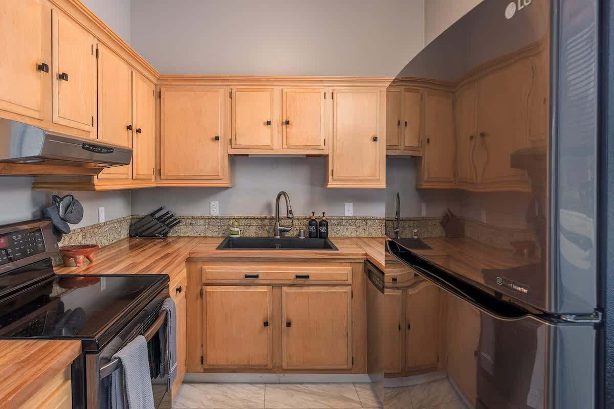 Cocina con armarios de madera, refrigerador de acero inoxidable y encimera negra.