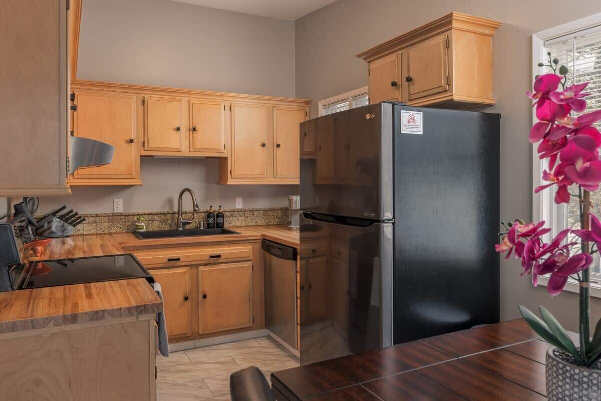 A kitchen with wooden cabinets, a stainless steel refrigerator, a sink, and a dining table.