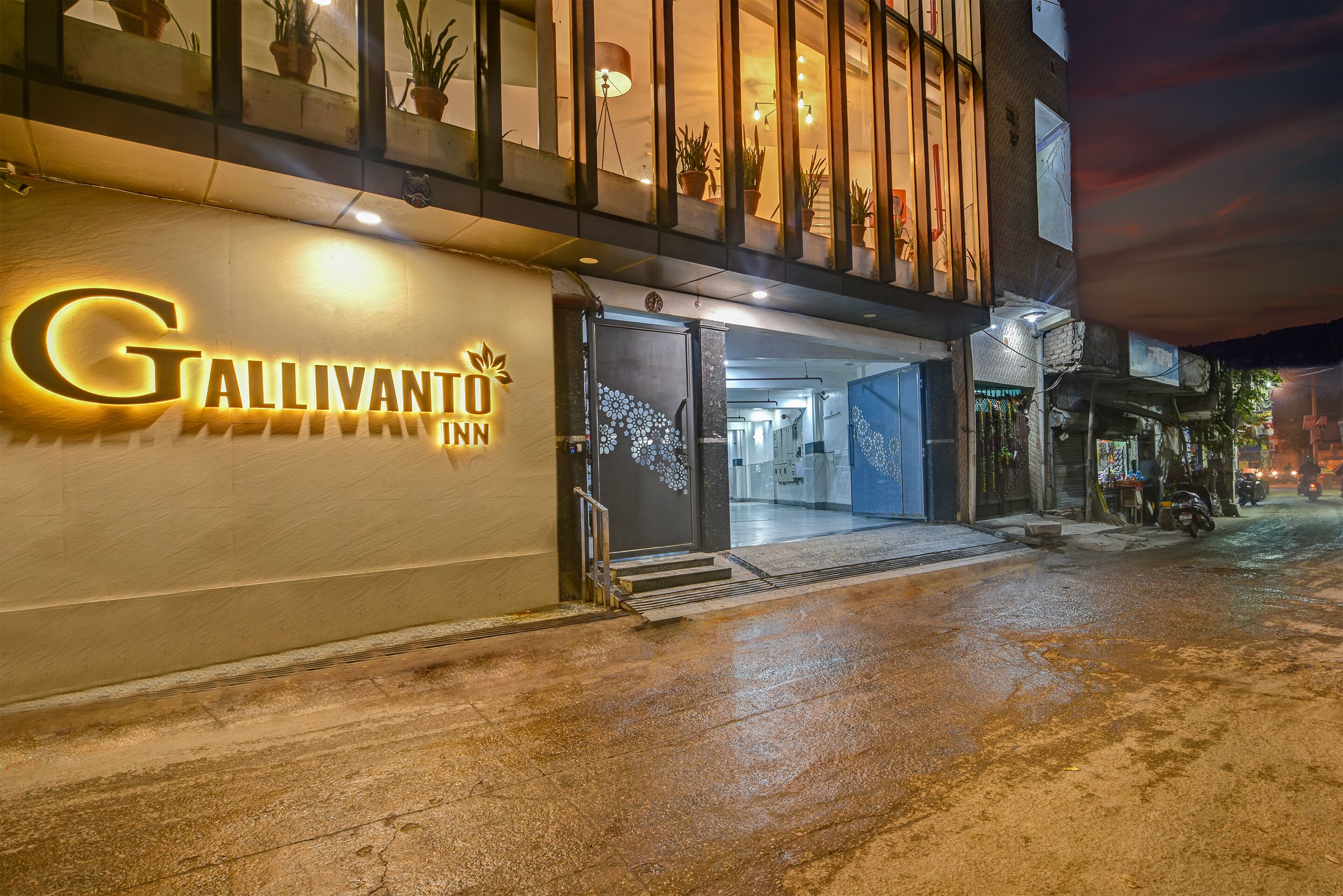 The exterior of the Gallivanti Inn with a prominent illuminated sign, a glass door entrance, and a wet pavement suggesting recent rain.