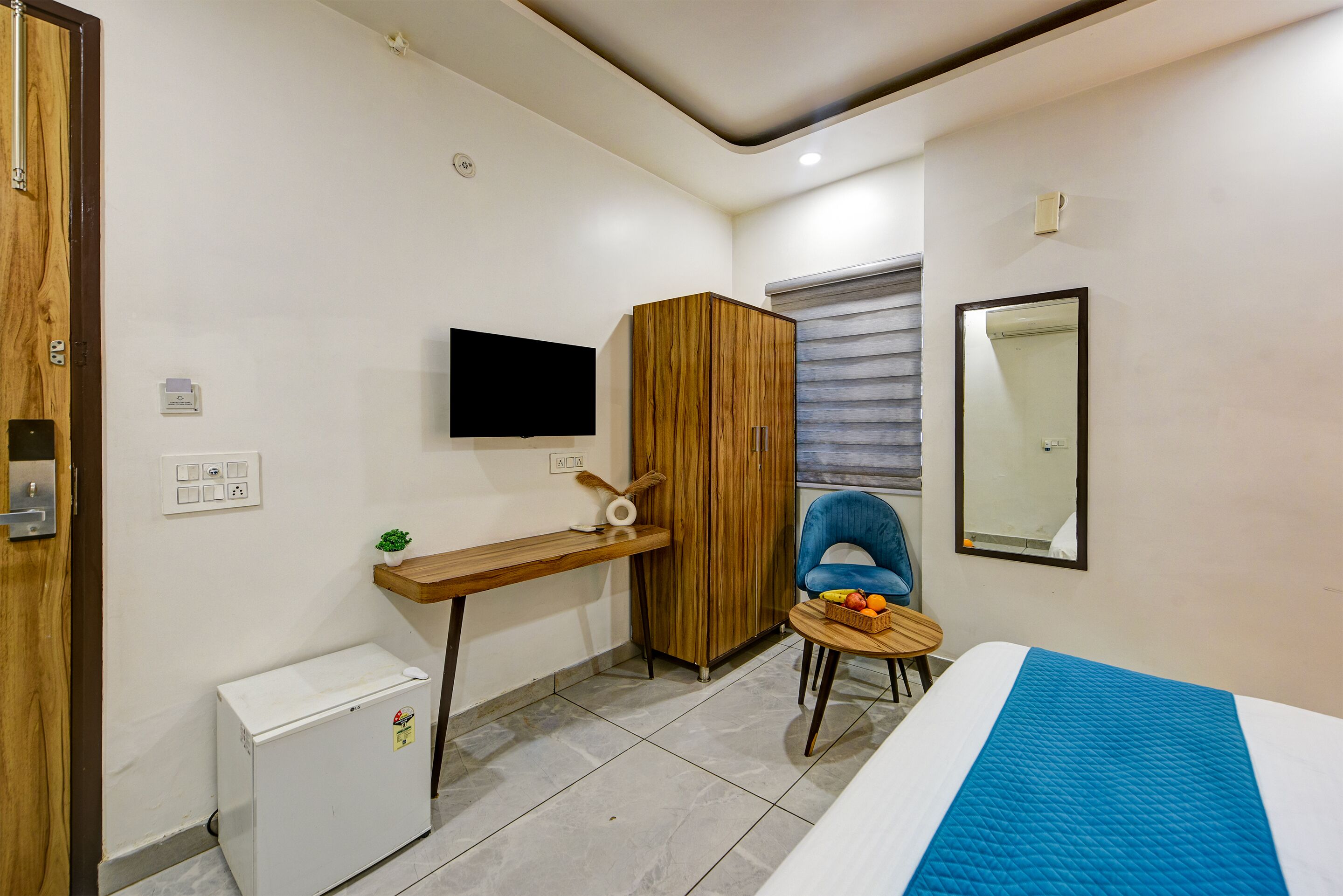 Una camera d'albergo compatta con un letto, una piccola scrivania, una sedia, un armadio, una televisione e una finestra con persiane.