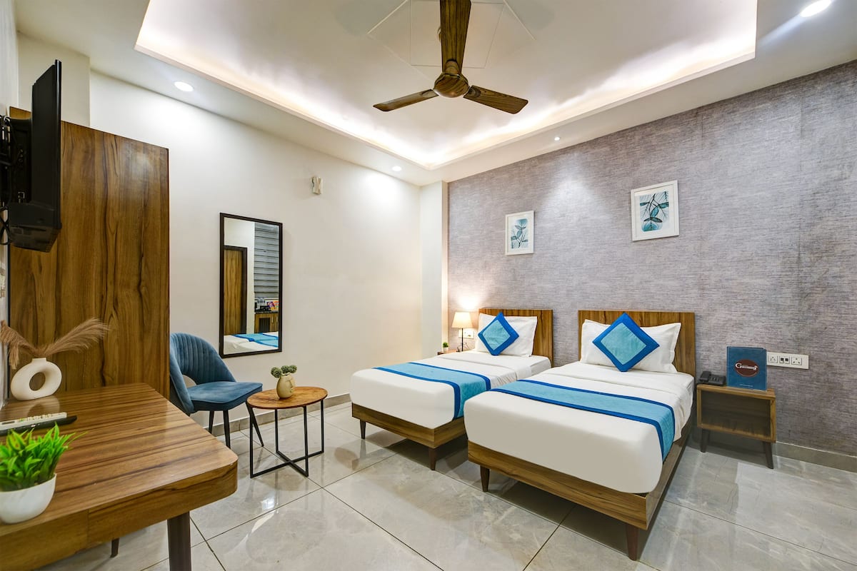 A hotel room with two beds, a desk, a chair, a ceiling fan, and artwork on the wall.