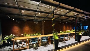 An outdoor dining area with long wooden tables and chairs, surrounded by potted plants and a patterned floor. - Gallivanto Inn (New Delhi)