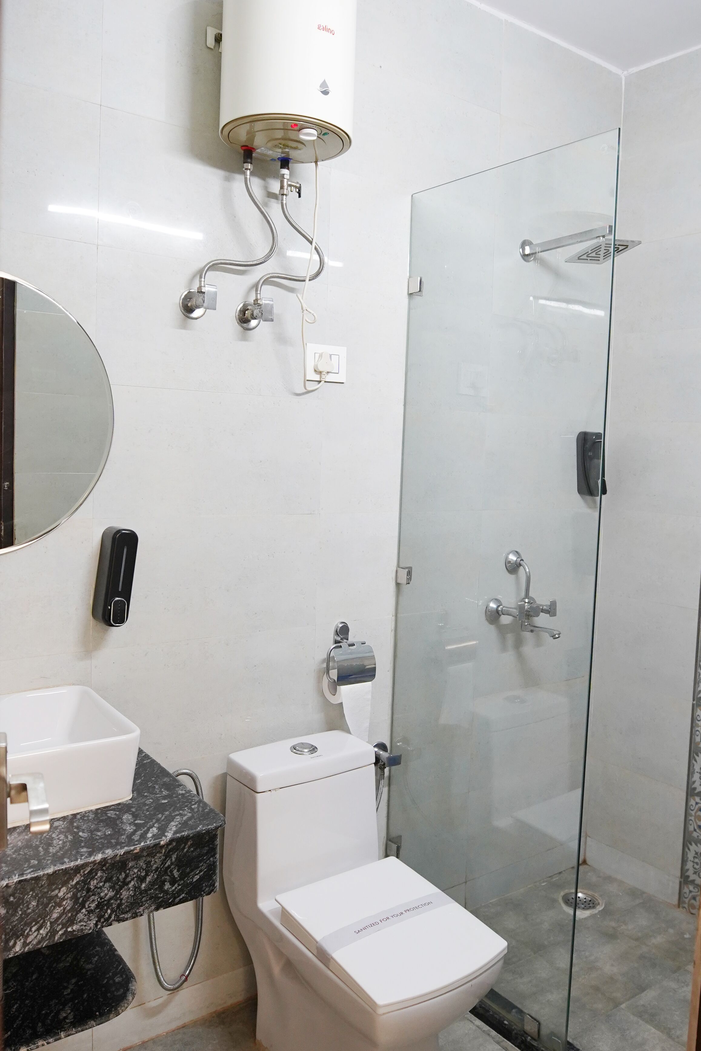 A modern bathroom with a glass shower enclosure, a white toilet, a sink with a marble countertop, and a round mirror.