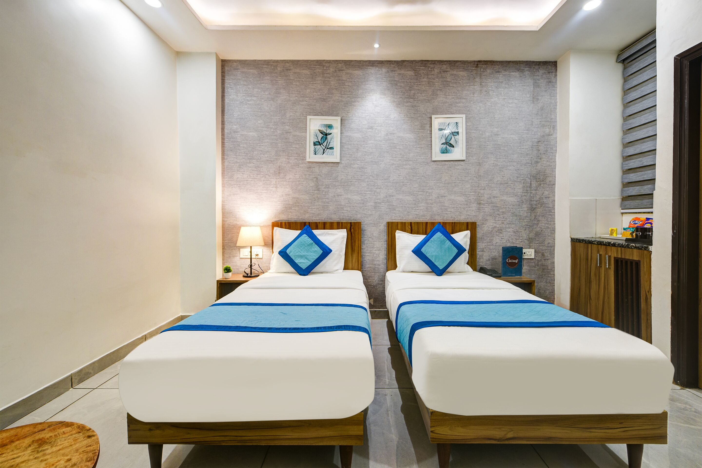 A hotel room with two beds, a nightstand, a lamp, and a wall-mounted coffee machine.