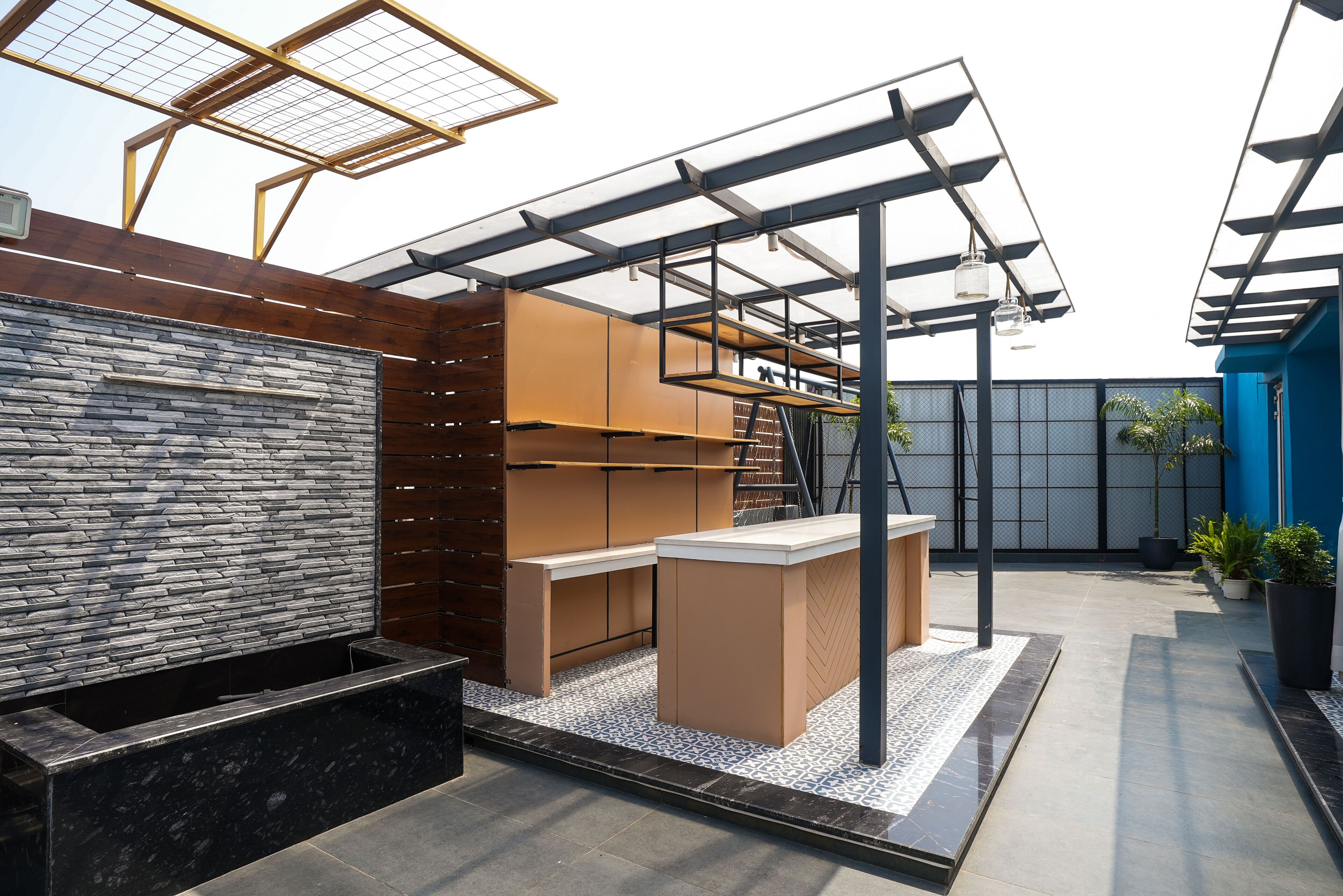 A modern outdoor seating area with a stone wall, wooden paneling, and a pergola with solar panels.