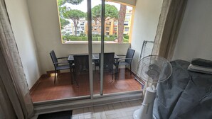 Un balcone con tavolo e sedie, una ventola e vista su edifici e alberi.