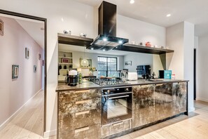 A modern kitchen with a central island, built-in oven, and a large range hood. - Notting Hill 2 Bed with Sauna - by Out of Office Lifestyle (London)