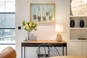 A modern room with a framed artwork of handbags, a vase with flowers, a lamp, and a view of the outdoors.