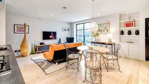 Una sala de estar moderna con sofá, mesa de comedor y sillas, un televisor de pantalla plana y un amplio ventanal.