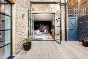 Une entrée étroite menant à une propriété dont la façade est en briques, avec une porte en verre et un plancher en bois.