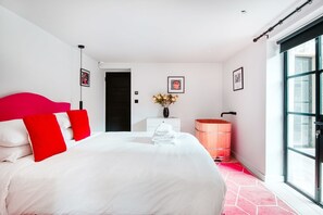 A modern bedroom with a large bed, a white dresser, a wooden barrel, and a large window. - Notting Hill 2 Bed with Sauna - by Out of Office Lifestyle (London)