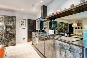 Une cuisine moderne dotée d’un grand îlot central, d’appareils électroménagers en acier inoxydable et d’un luminaire suspendu.