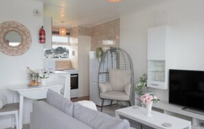 A modern living room with a grey sofa, a hanging chair, a flat-screen TV, and a white cabinet.