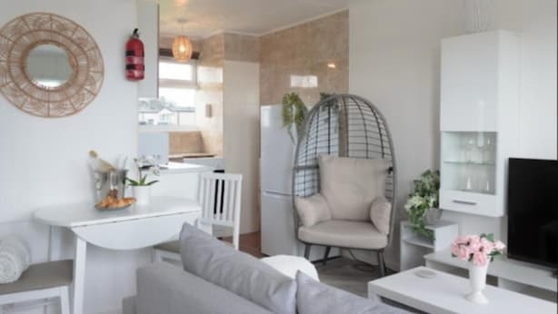 Una sala moderna con sofá, mesa de comedor, zona de cocina y una silla colgante.