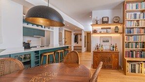Een moderne keuken met blauwgroene kastjes, een houten eettafel en een grote boekenkast vol boeken.