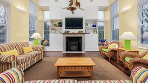 Ein Wohnzimmer mit Kamin, gestreiften Sofas, Korbstühlen und einem flachbildfernseher, der über dem Kamin angebracht ist.