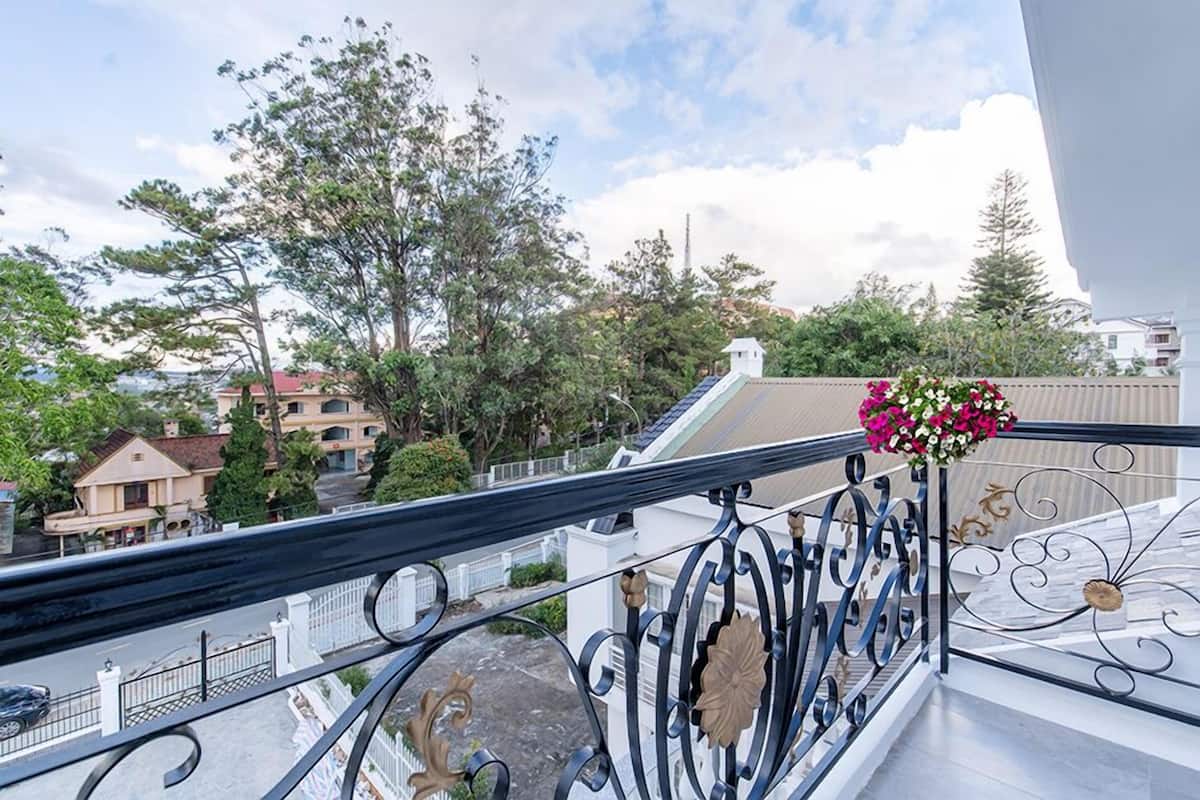 A balcony with a metal railing, a flower arrangement, and a view of the street and buildings.