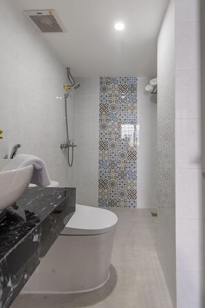 Um banheiro moderno com vaso sanitário branco, pia de mármore e chuveiro com parede de azulejos estampados.
