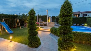 Un giardino con piscina, uno scivolo e una zona patio con illuminazione esterna.