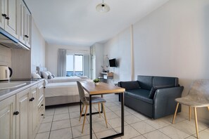 A modern hotel room with a bed, a dining table, a sofa, and a TV.