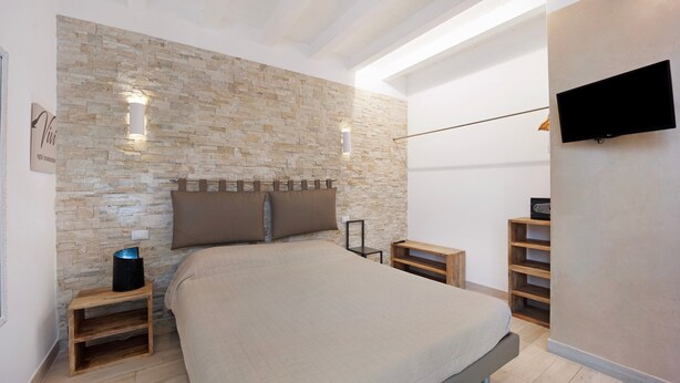 A bedroom with a stone wall, a bed, a TV, and a wooden nightstand. - 'Ama' Apartment with Balcony, Wi-Fi, and Air Conditioning (Albenga)