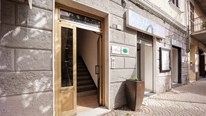 A building with a staircase leading to an entrance, a signboard, and a large planter on the sidewalk. - 'Ama' Apartment with Balcony, Wi-Fi, and Air Conditioning (Albenga)