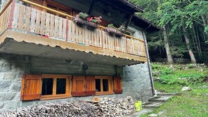 Un bâtiment en pierre doté d’un balcon en bois, de fenêtres avec volets et d’une pile de bois de chauffage.